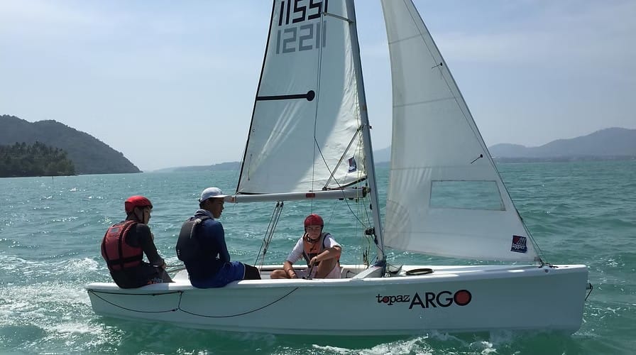Three sailors aboard a Topper Argo dinghy during practical sailing training in tropical waters with Java Yachting.