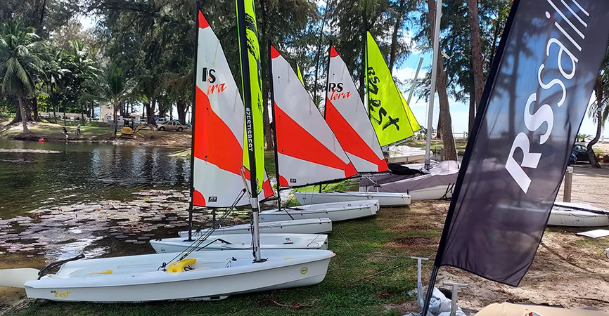 Selection of RS sailing dinghies including RS Tera, RS Feva and RS Zest boats displayed beside the water.