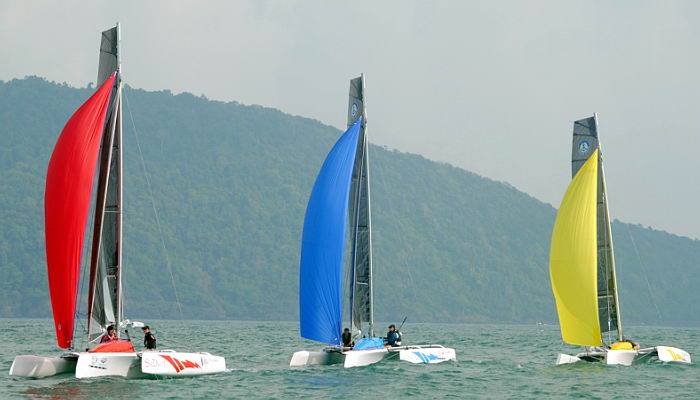 Three Pulse 600 performance trimarans sailing with colourful red, blue and yellow sails in tropical waters.