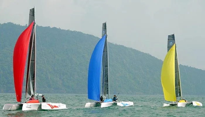 Three Pulse 600 performance trimarans sailing with colourful red, blue and yellow sails in tropical waters.