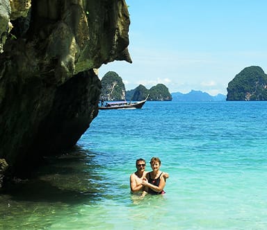 Guests swimming in crystal clear turquoise water beside dramatic limestone islands during a tropical yacht charter in Thailand.