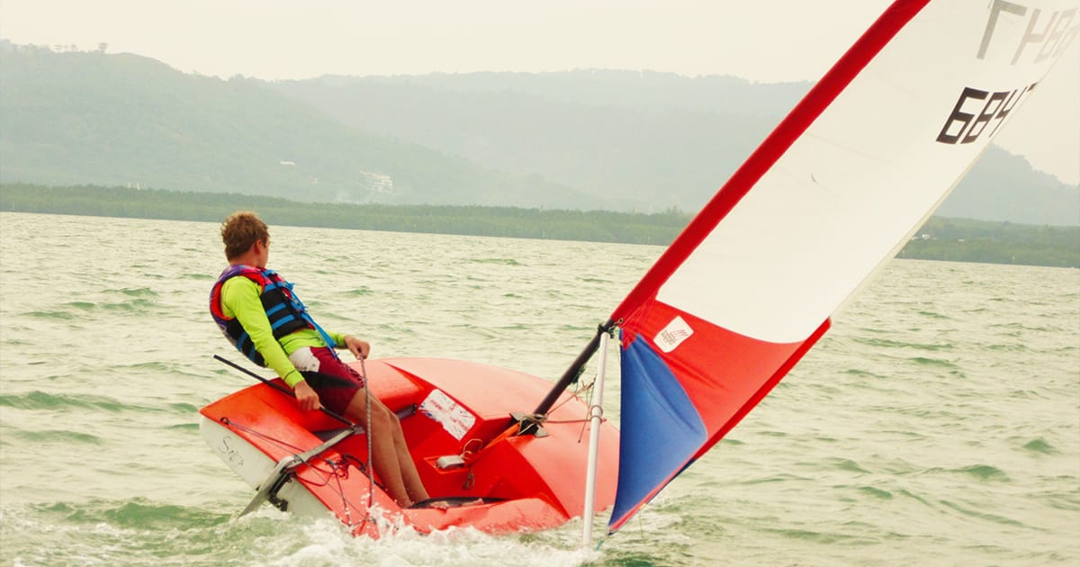 Single sailor handling a red Topper dinghy on open water during a Java Yachting sailing course in Thailand.