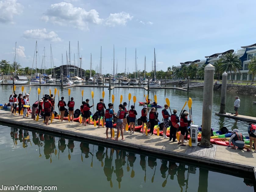 Students wearing buoyancy aids preparing kayaks and paddles at a marina before a Java Yachting activity