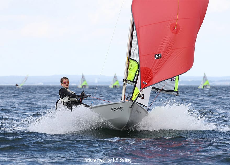 RS Feva double-handed performance sailing dinghy planing through waves with red asymmetric spinnaker.
