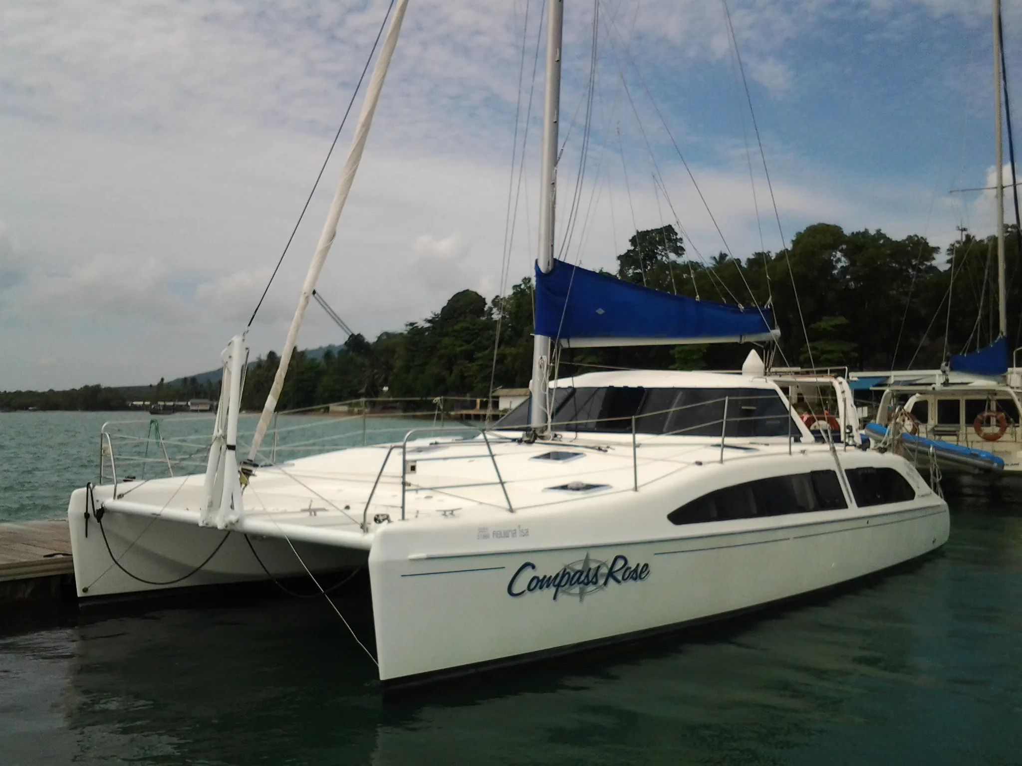 Compass Rose cruising sailing catamaran anchored beside a tropical limestone island in Thailand.